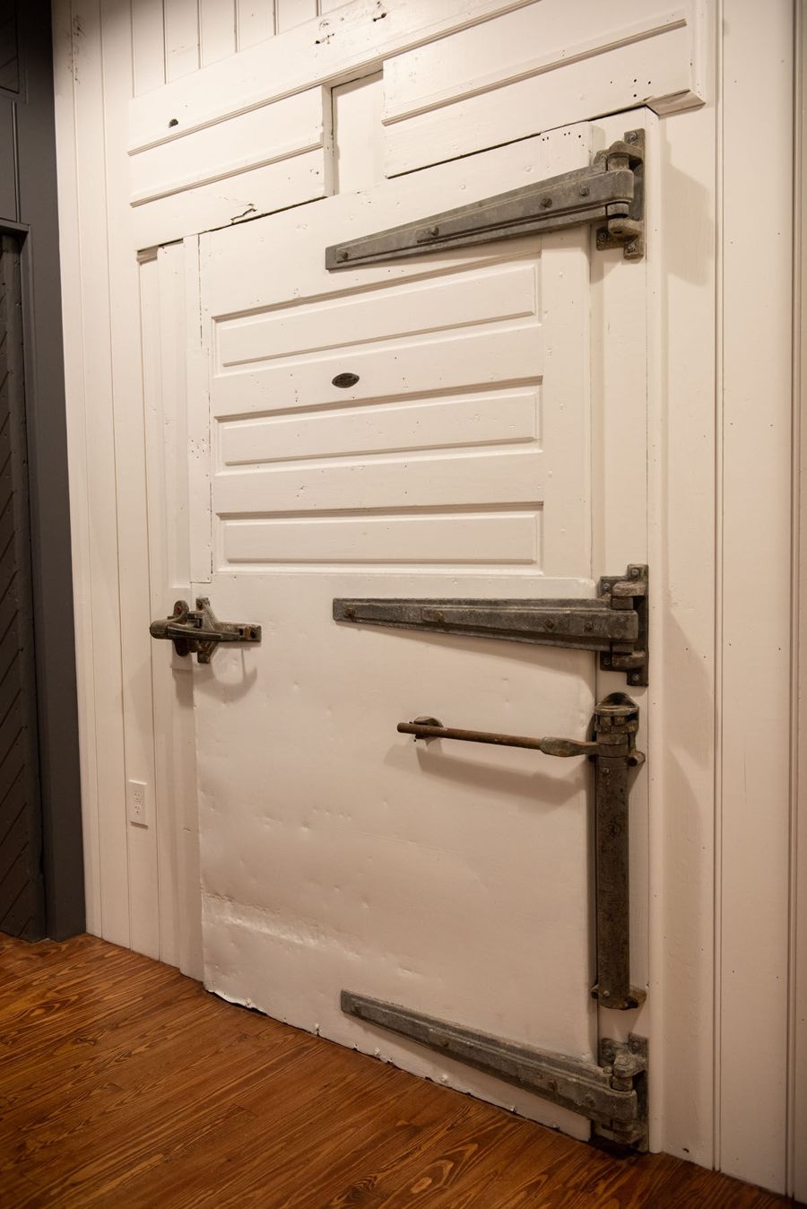 A salvaged white cold-storage door with its original heavy iron hinges and latch