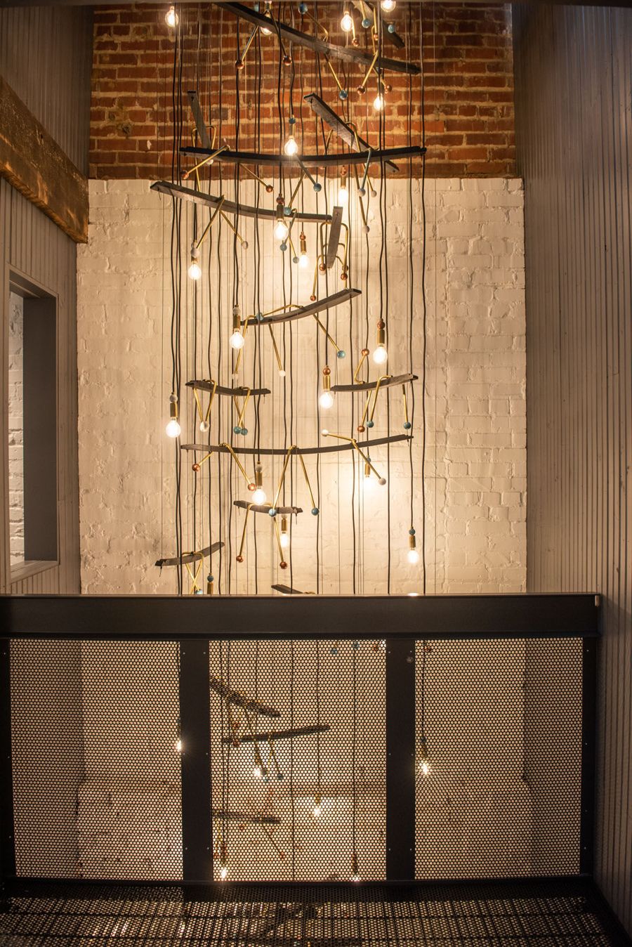 A cascading chandelier of branches and bulbs hanging through a brick lightwell above a steel railing