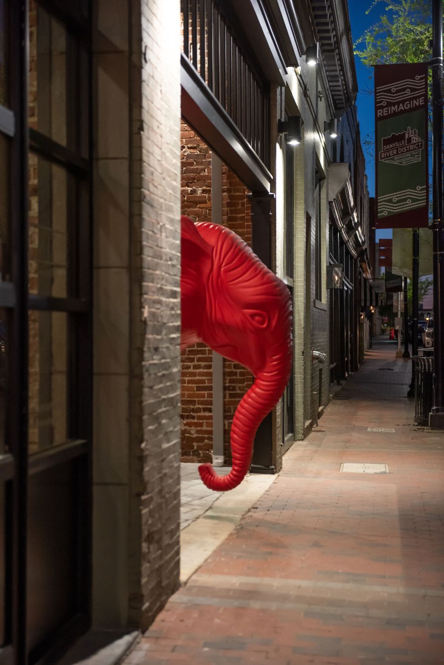 Red elephant sculpture peeking out from the building entrance onto the Craghead Street sidewalk at dusk