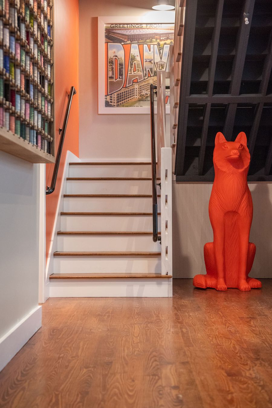 Orange accent wall and staircase with a vintage Danville postcard print and an orange fox sculpture at the foot of the stairs