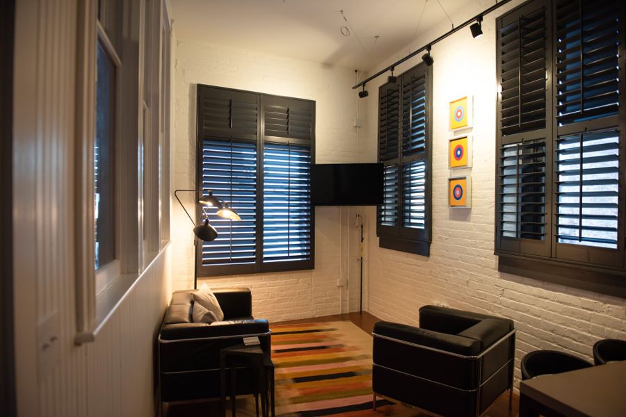 Living room with black leather seating, a striped rug and bullseye prints on white brick