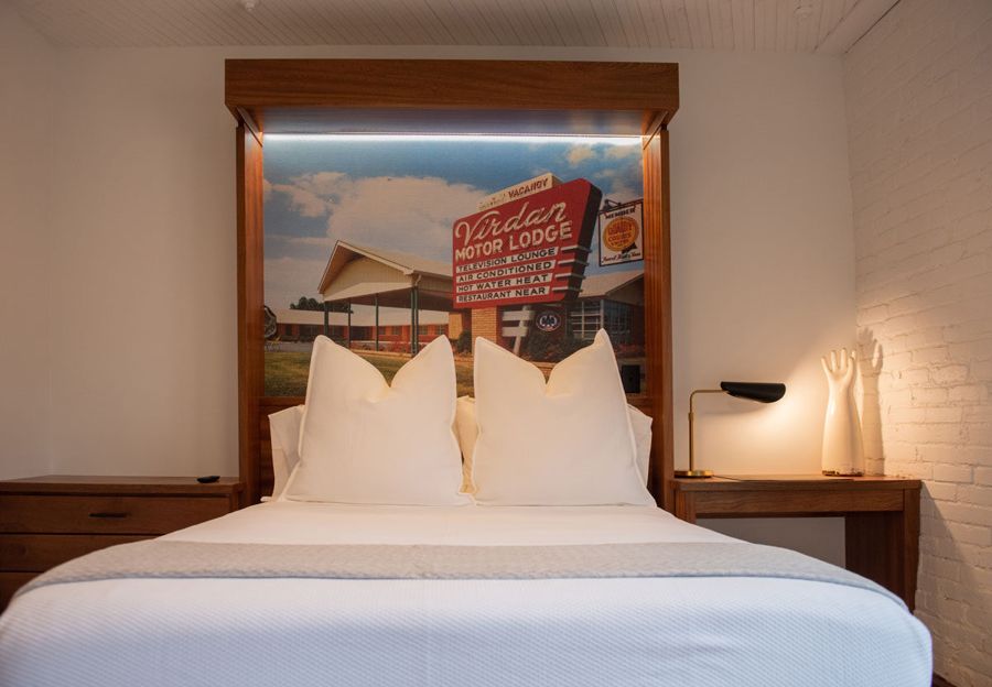 Bed with a backlit sapele headboard framing a vintage postcard of the Virdan Motor Lodge