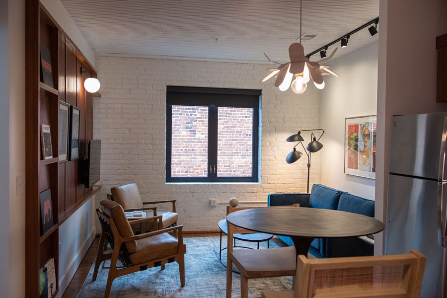 Open living and dining area with leather armchairs, a blue velvet sofa, a petal pendant light and white brick walls