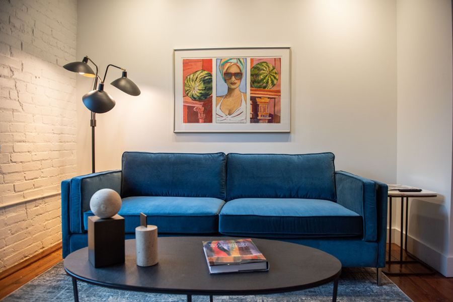 Blue velvet sofa beneath a framed painting of a woman in sunglasses between two watermelons