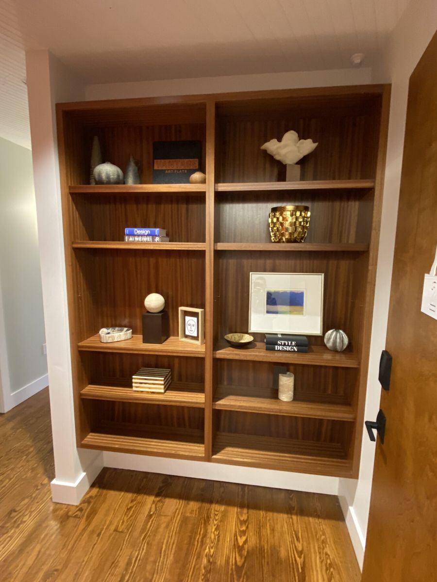 Sapele wood built-in shelves in the entry styled with ceramics, art books and a framed print