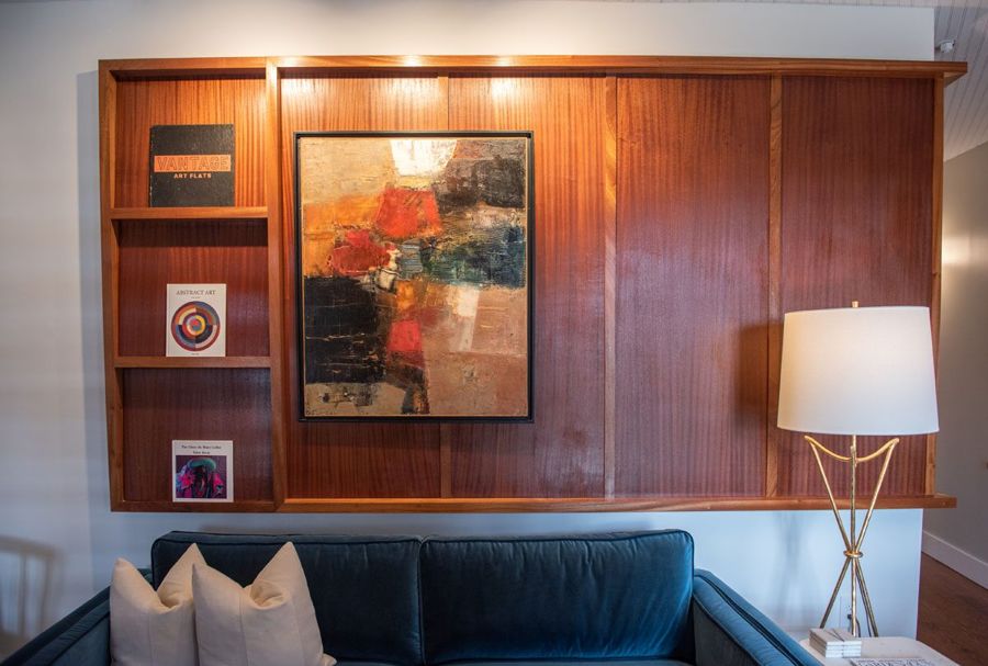 Sapele wood gallery wall with an abstract oil painting and art books above a blue velvet sofa