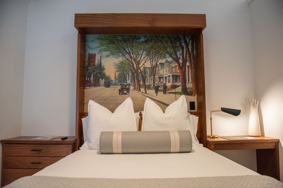 Bed with a sapele headboard framing a vintage postcard of a tree-lined Danville street with a streetcar