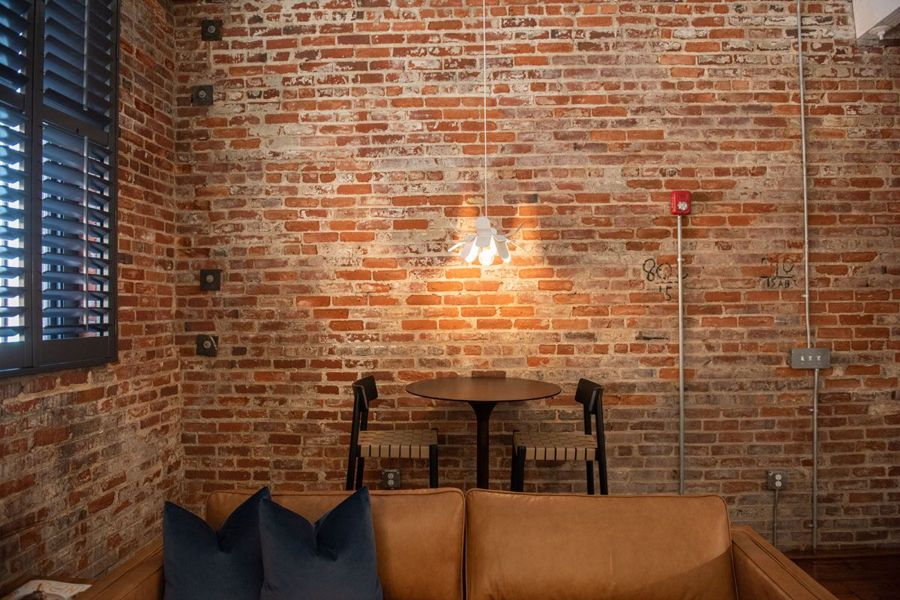 Round bistro table with woven-seat chairs beneath a petal pendant light against an original brick wall