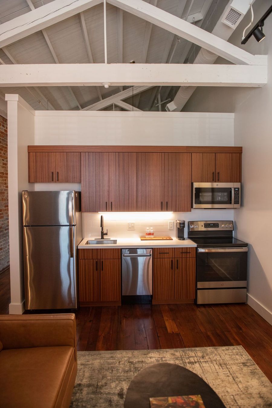 Kitchen with sapele wood cabinetry and stainless steel appliances beneath white exposed roof beams