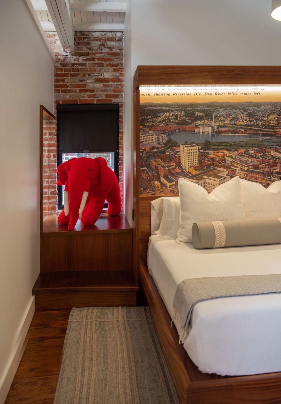 Sapele window bench set into exposed brick beside the bed, with a red plush elephant