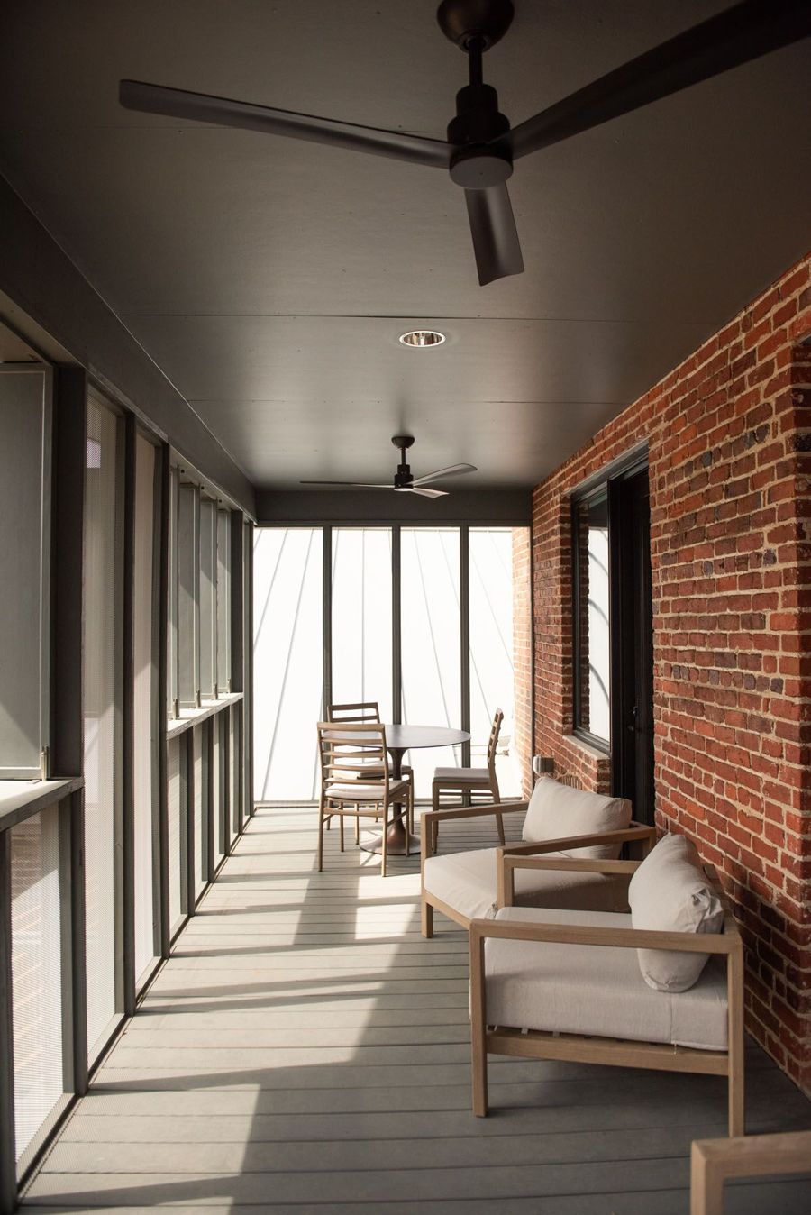 Private screened rear porch with lounge chairs, a bistro table and a ceiling fan along the exposed brick wall