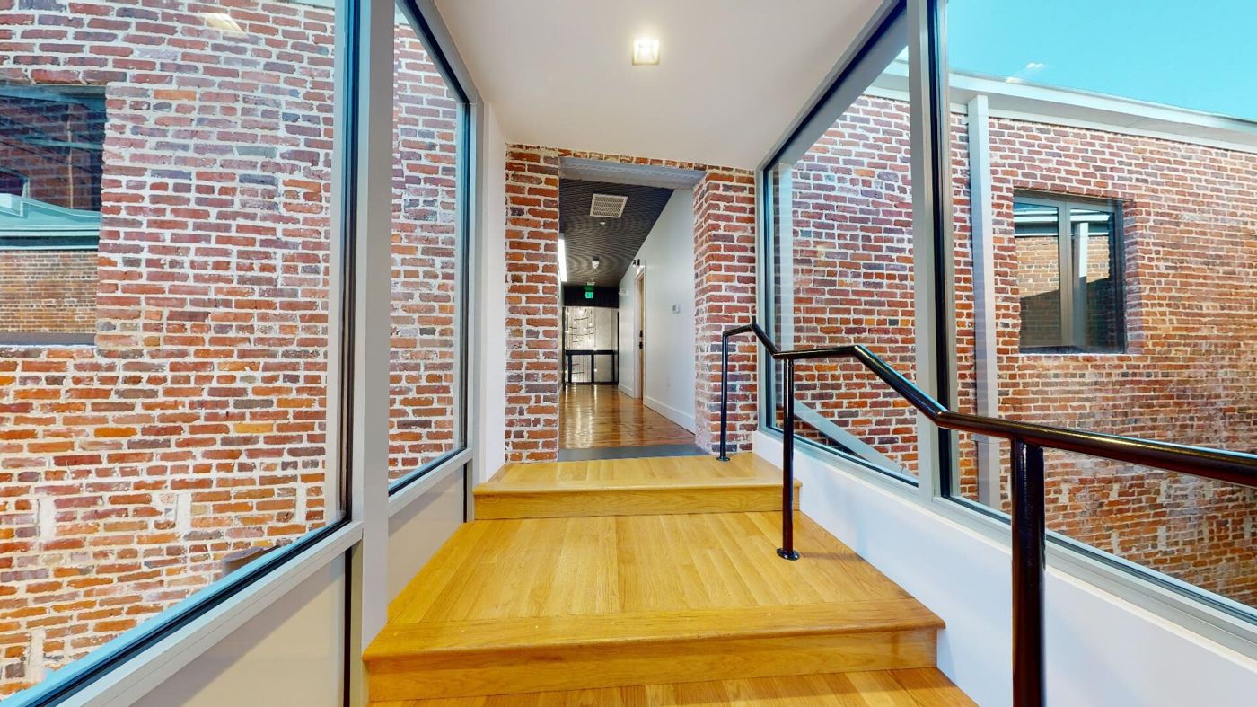 Inside the glass-walled bridge connecting the two buildings, with steps leading up between exposed brick walls