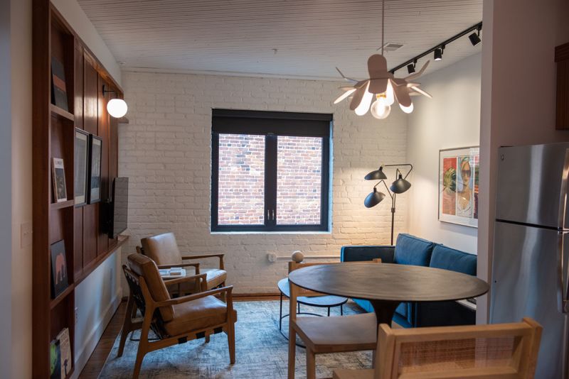 Open living and dining area with leather armchairs, a blue velvet sofa, a petal pendant light and white brick walls