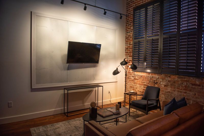 Living room with a cognac leather sofa, black armchair, tripod floor lamp and shuttered windows set into exposed brick